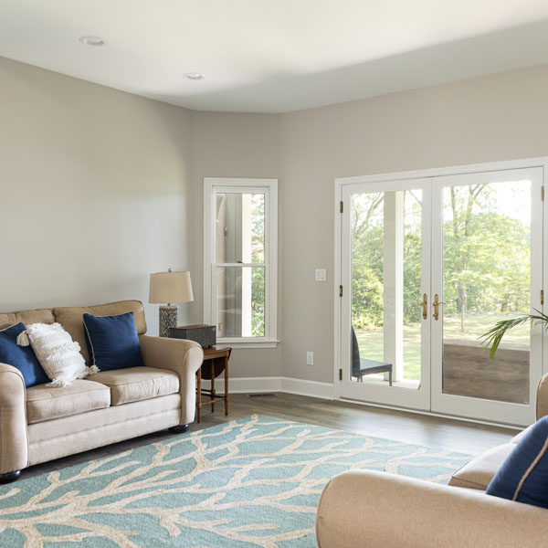 A living room with two sofas, nautical-themed area rug and sweeping water views through the french doors and windows.