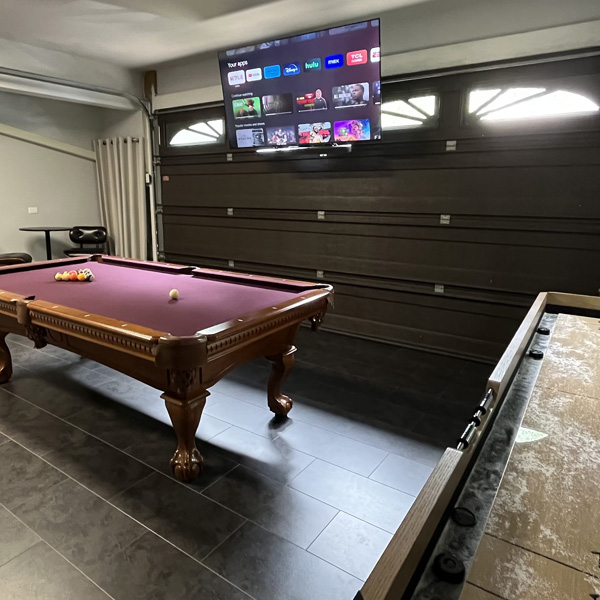 A pool table, shuffleboard table, and large Smart TV are in the garage game room at The Nest at Swan Point Virginia Airbnb vacation rental.