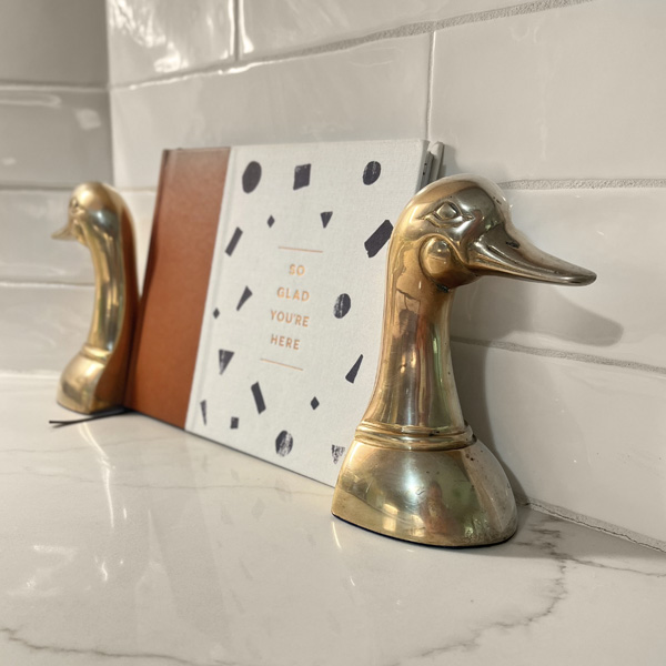 Two gold swan bookends hold a guestbook with text on the front, that reads, "So Glad You're Here."
