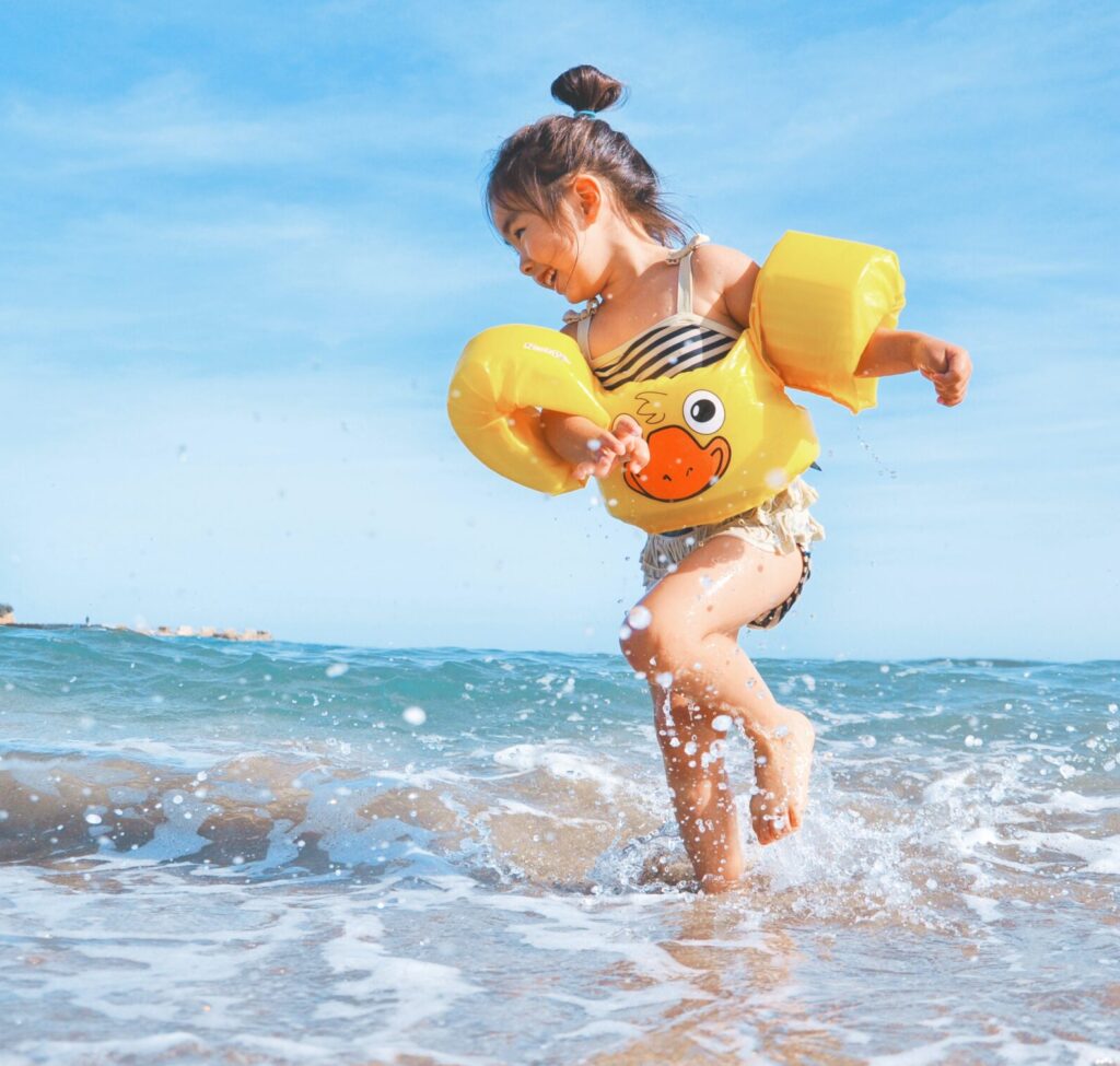 A young, happy girl wearing water-wings runs through the surf on a beach.